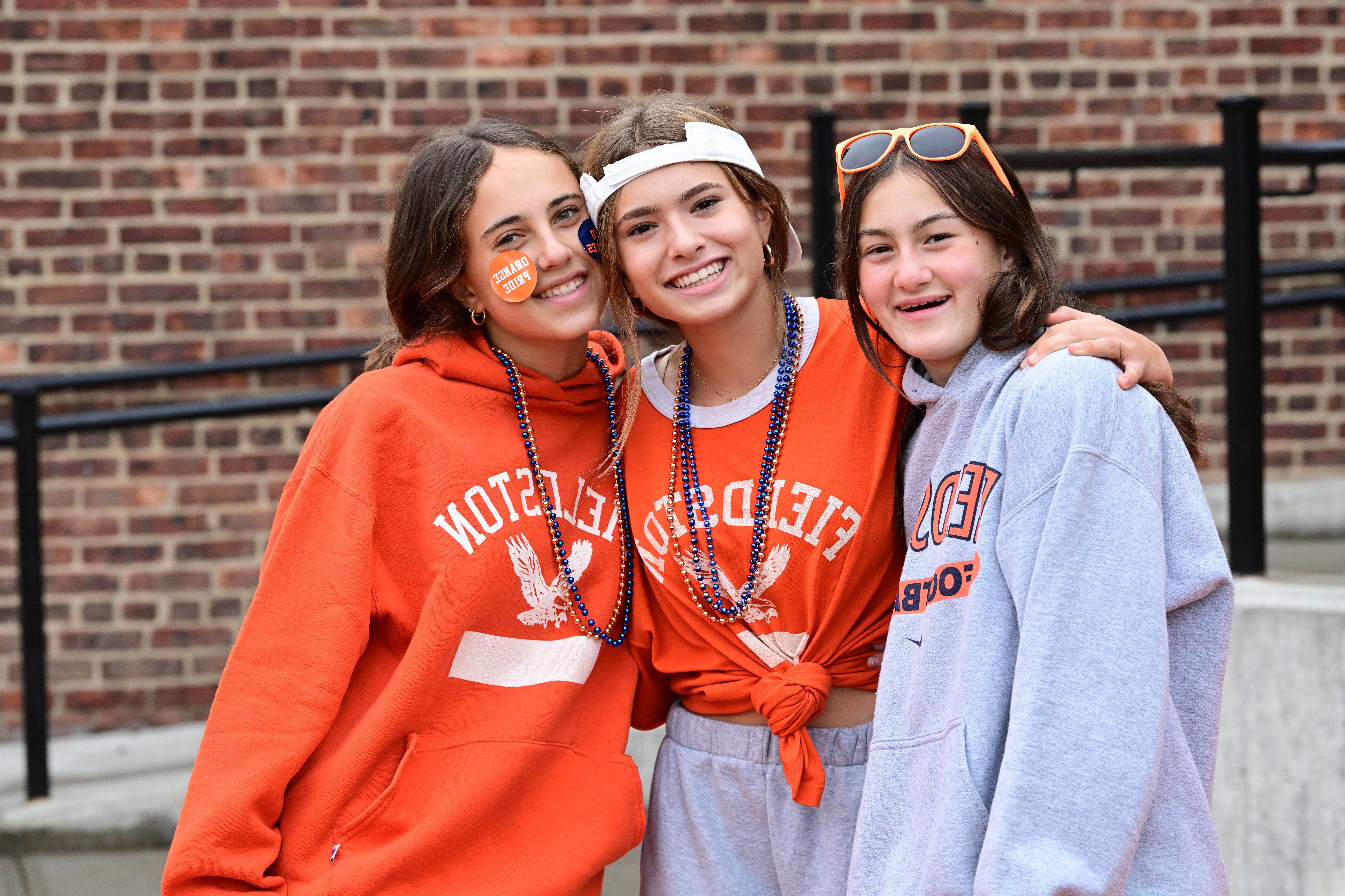 三个学生穿着ECFS的橙色衬衫摆姿势