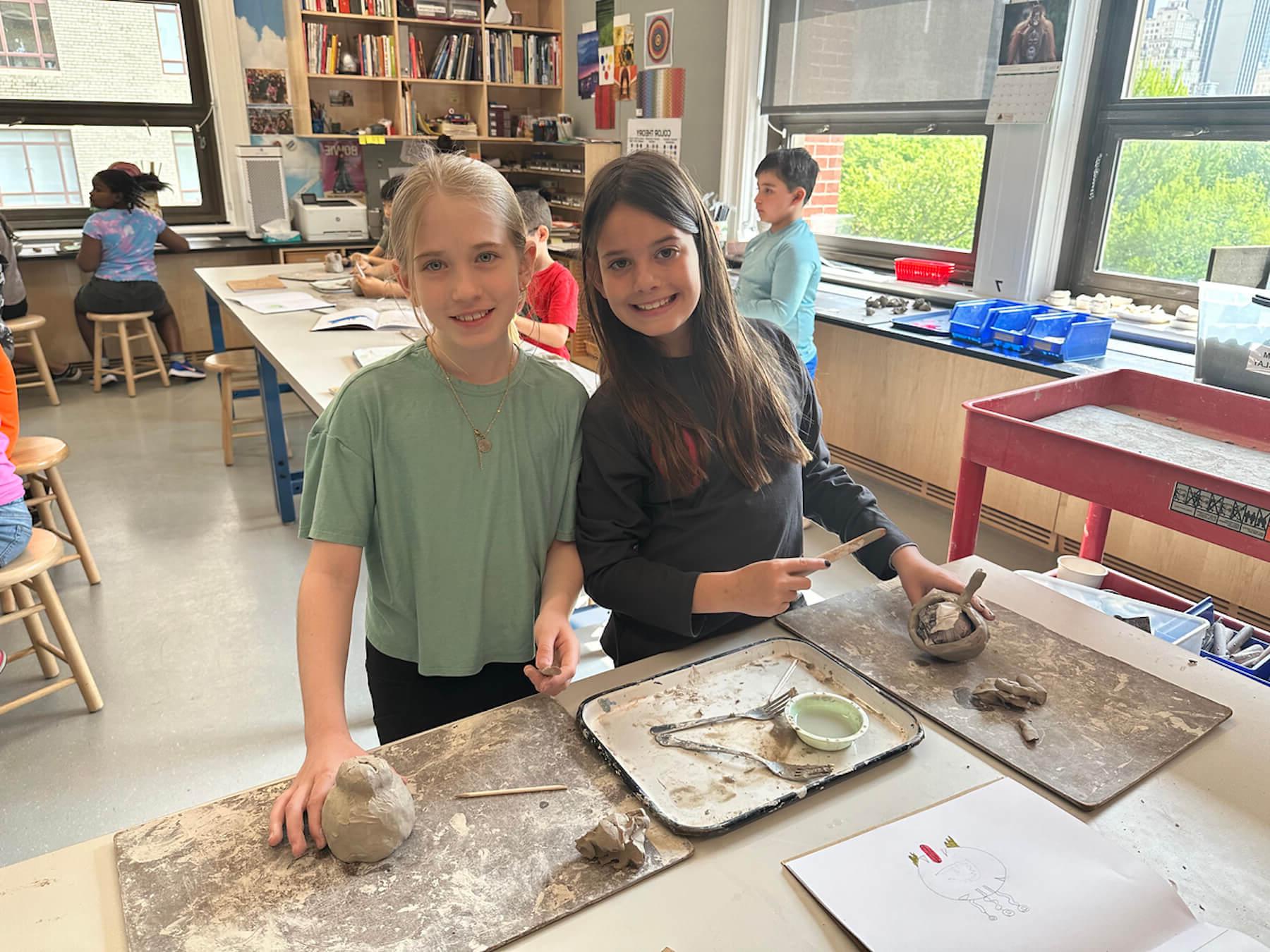 二年级学生在艺术教室里与他们的陶艺作品合影微笑.