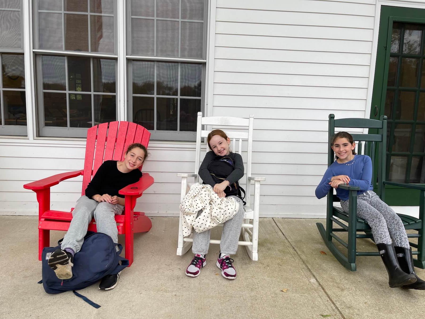 Three Ethical Culture students gather on porch, smiling from rocking chairs.