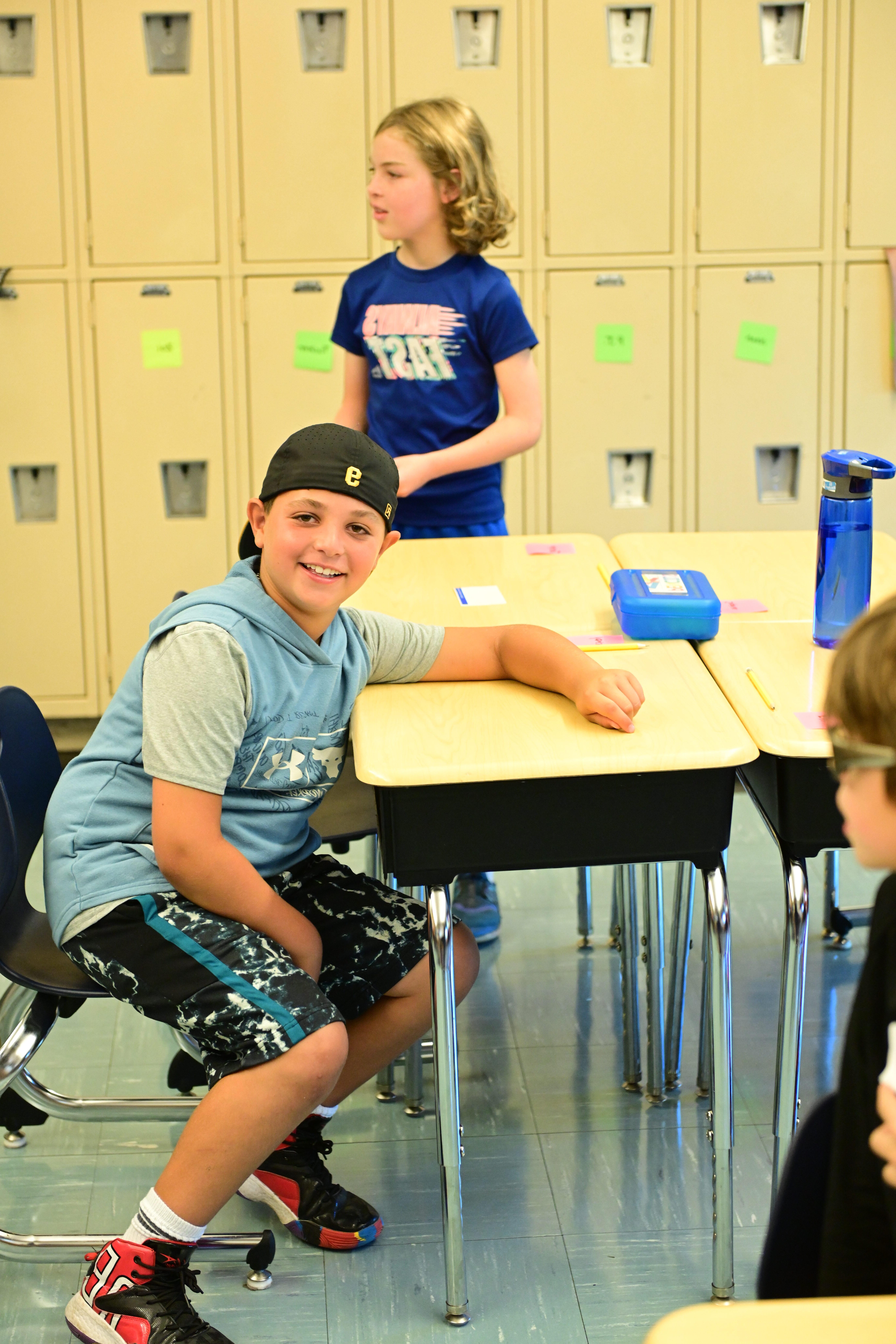 一名学生坐在菲尔德斯顿小学教室的课桌前，对着镜头微笑
