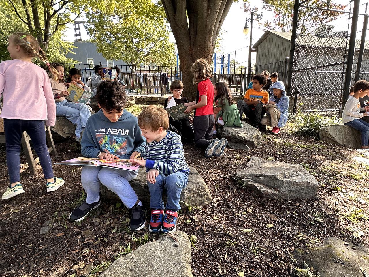 两个菲尔德斯顿低年级的学生坐在菲尔德斯顿低年级花园的一块岩石上一起读书.