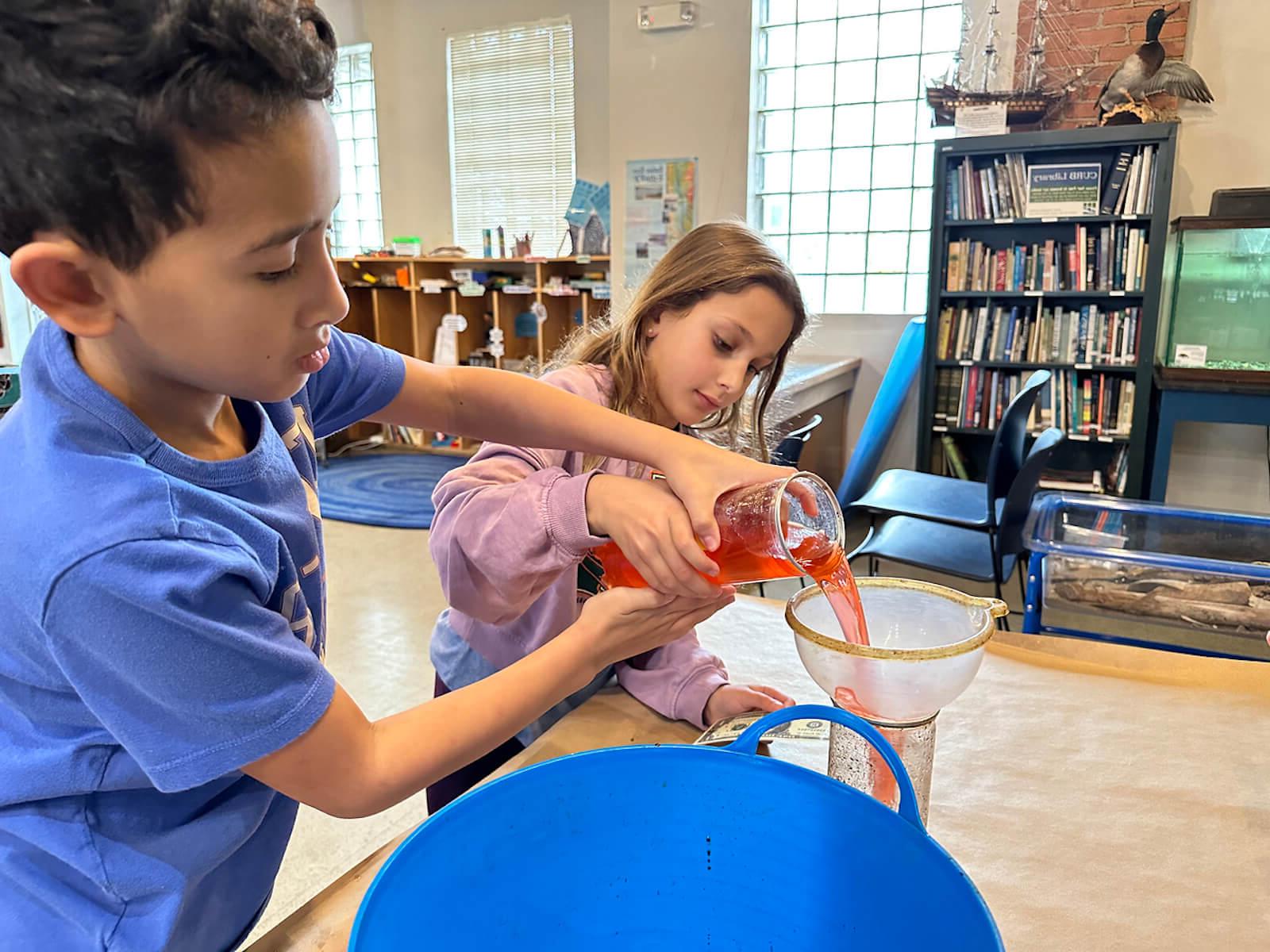 Two Fieldston Lower students pour water into a filter at the Beczak Center.