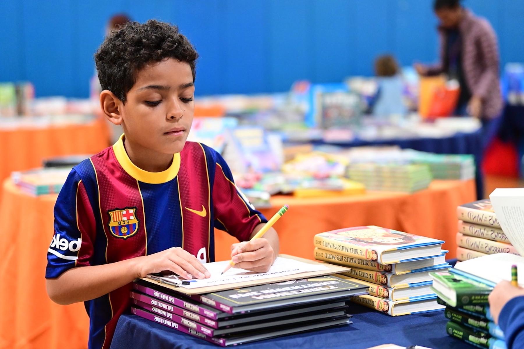 Fieldston Lower students writes down the name of a book using a pencil at the book fair.