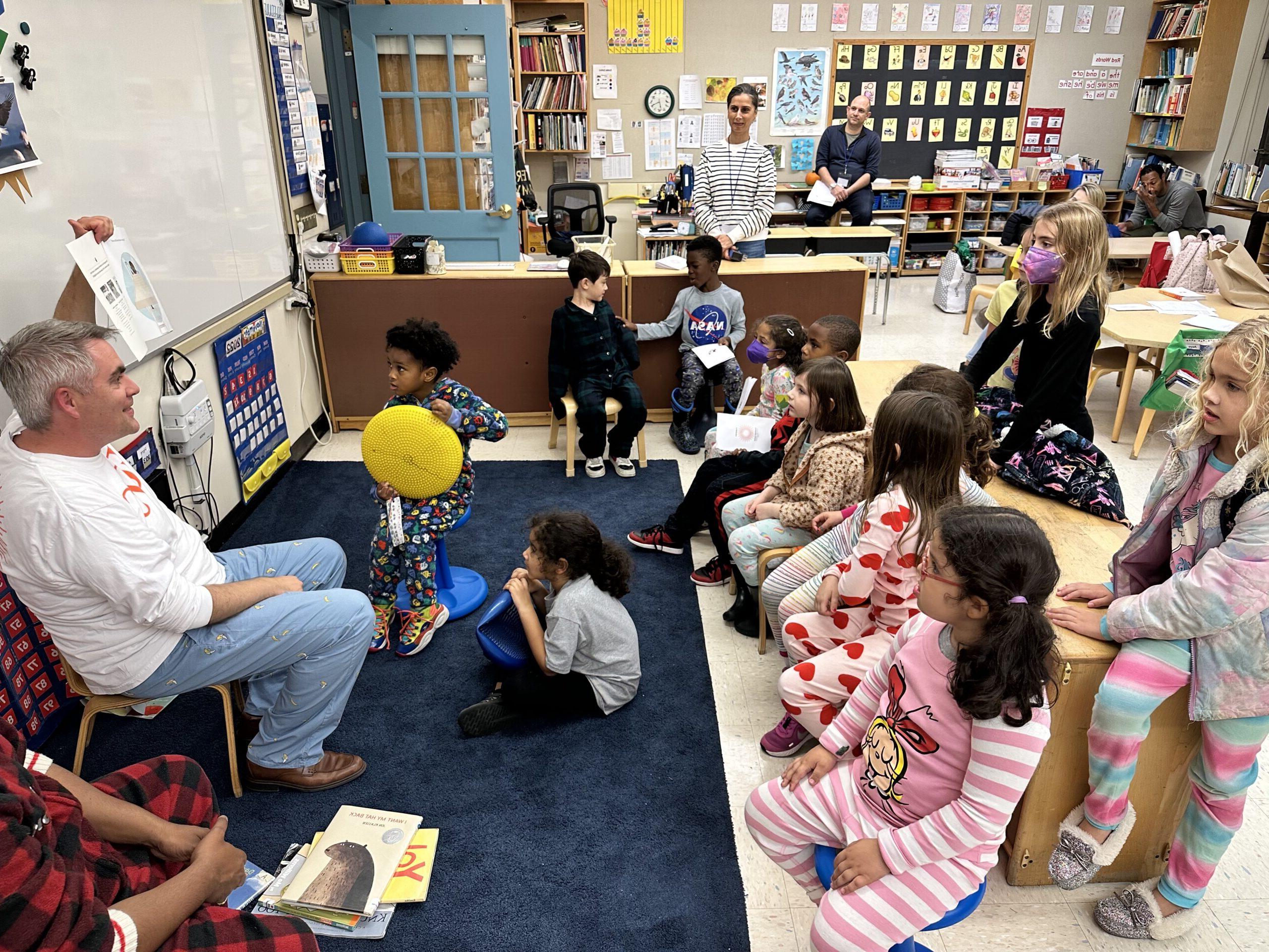 Fieldston Lower Principal Joe McCauley reads to a room full of students; they sit on the floor in pajamas and listen along.