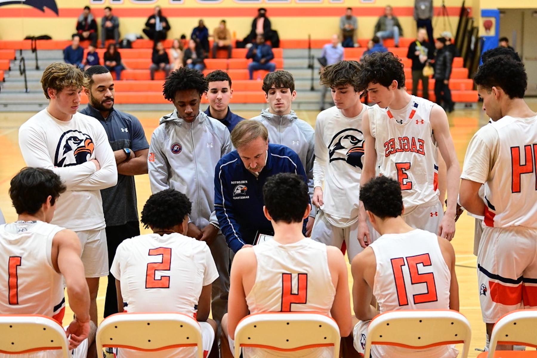 Fieldston Upper boys varsity basketball players huddle around the bench and listen as their coach draws out a play.