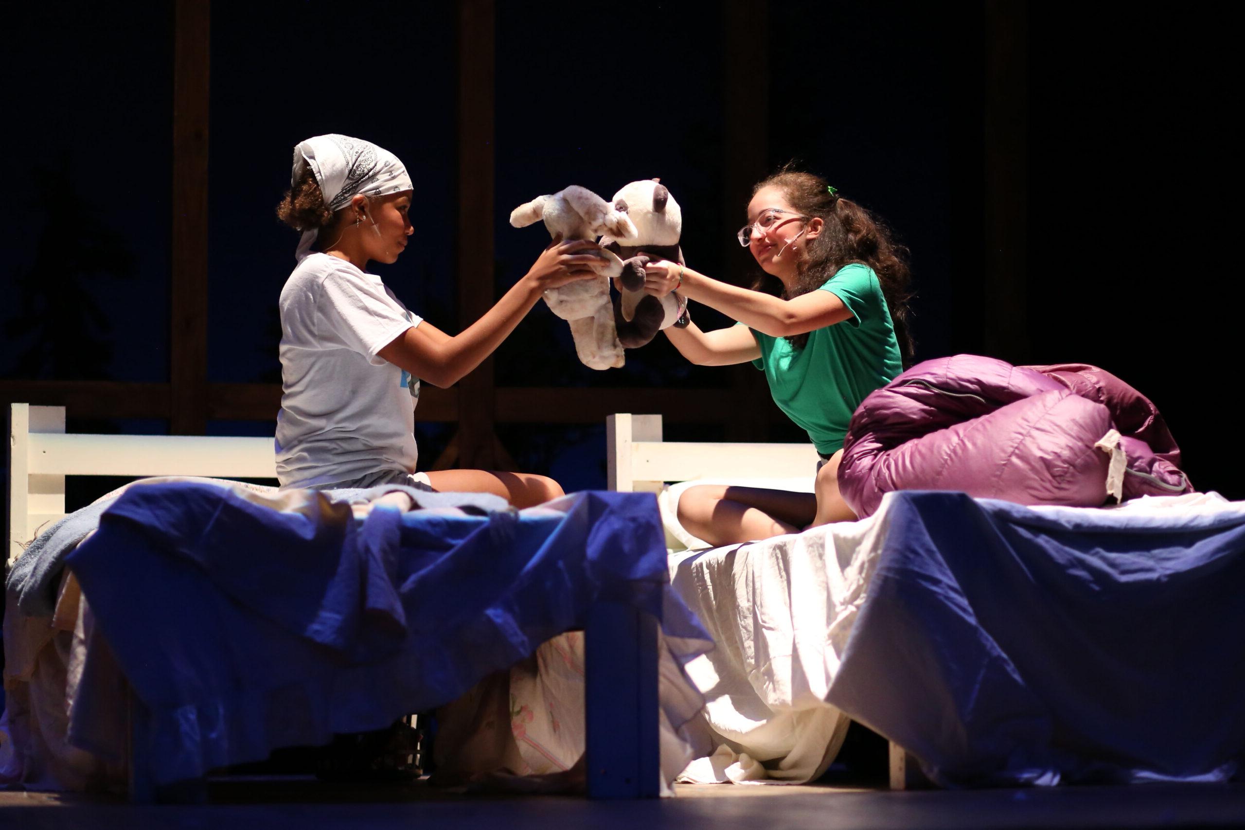 Fieldston Upper students sitting on beds, holding up stuffed animals, while on stage during the fall drama theatre production at the Ethical Culture Fieldston School